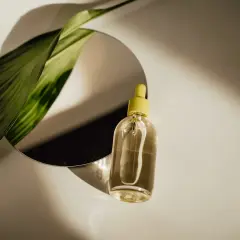 Szklana buteleczka z żółtą pipetką i zielony liść odbijają się w lustrze. Czy serum się zmywa? Naturalne piękno w kropli.