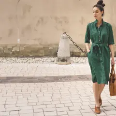 Elegancka kobieta w zielonej lnianej sukience prezentuje letnie stylizacje do biura, idąc ulicą z brązową torbą.