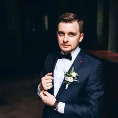 Elegancki mężczyzna w granatowym garniturze, z butonierką i muszką. Idealny przykład, jak dobrać garnitur na specjalną okazję.