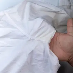 Dłoń pokazuje białą koszulę z żółtymi, twardymi plamami po antyperspirancie pod pachą.