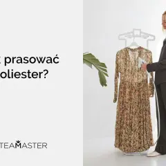 Kobieta pokazuje, jak prasować poliester za pomocą parownicy. Długa, kwiecista sukienka wisi na wieszaku.