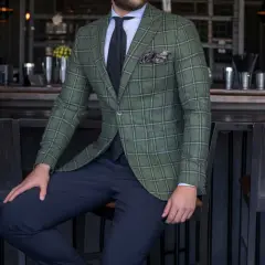 Elegancki mężczyzna w marynarce w kratę w kolorze butelkowej zieleni. Granatowe spodnie i czarny krawat.