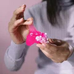 Różowy slime z białymi kuleczkami w dłoniach. Dowiedz się, jak usunąć slime z ubrania, zanim zaschnie.