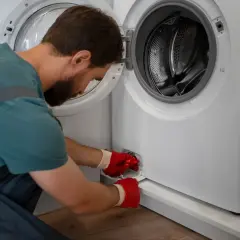 Mężczyzna w czerwonych rękawiczkach otwiera klapkę pralki, by sprawdzić, czym wyczyścić gumę.