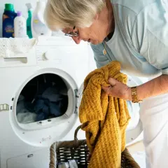 Starsza pani wyjmuje z pralki żółty sweter, martwiąc się, czy nie pojawiły się na nim plamy po płynie do płukania.