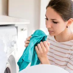 Kobieta wącha świeżo wyprane ubranie, zastanawiając się, dlaczego pranie śmierdzi po wysuszeniu.