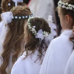 Dziewczynki w białych strojach z pięknymi fryzurami komunijnymi z wiankiem z kwiatów i wstążek.