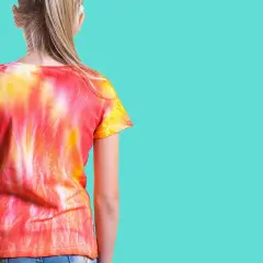 Dziewczynka w koszulce tie-dye w odcieniach czerwieni i żółci. To znaczy, że wzór powstał przez wiązanie i farbowanie materiału.