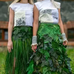 Dwie kobiety prezentują ekologiczną modę z recyklingu. Jedna w spódnicy z trawy, druga w sukni z liści.