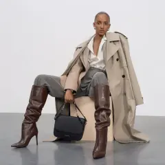 Elegancka stylizacja: jak nosić koszulę oversize z trenczem, szarymi spodniami i brązowymi kozakami.