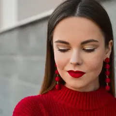 Elegancka fryzura do czerwonej sukienki, podkreślona złotym makijażem oczu i wyrazistymi, czerwonymi kolczykami.