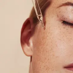 Kropla serum z pipetki spada na piegowatą skórę. Dowiedz się, jak stosować retinol dla pięknej cery.