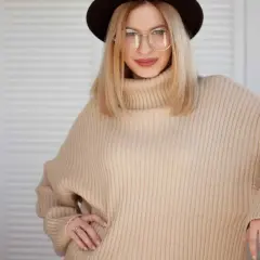 Kobieta w beżowym swetrze oversize i okularach, prezentująca stylowe, luźne ubrania.