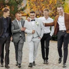 Pięciu mężczyzn w eleganckich stylizacjach na wesele, idących razem i rozmawiających.