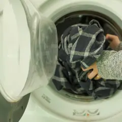 Ręce wkładają kratkowaną koszulę do pralki. To będzie czyste pranie z octem.