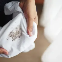 Dłonie trzymają białą tkaninę z widocznymi, **starymi tłustymi plamami na ubraniach**.