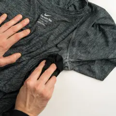 Dłonie czyszczą ciemną koszulkę Nike, by pozbyć się zapachu potu. Skuteczny sposób na świeżość ubrań sportowych.