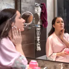 Kobieta w szlafroku aplikuje krem z filtrem SPF w ciąży, dbając o skórę twarzy przed lustrem.
