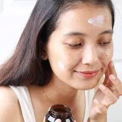 Kobieta aplikuje krem Purito Panthenol Cream na twarz, dbając o nawilżenie skóry.