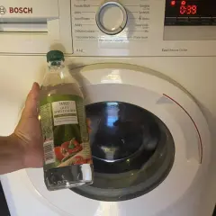 Dłoń trzyma butelkę octu spirytusowego przy pralce Bosch. Ocet do pralki to świetny sposób na odświeżenie bębna.