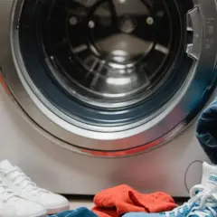 Przed pralką leżą buty i ubrania. Zastanawiasz się, w jakiej temperaturze prać bieliznę? Sprawdź metkę!