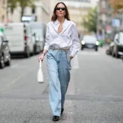 Kobieta w luźnych jeansach i białej koszuli, z białą torebką. To jest właśnie ten styl, który można nazwać "mom fit".