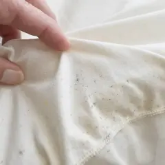 Dłoń pokazuje biały materiał z widocznymi, nieestetycznymi, tłustymi plamami na ubraniach po praniu.