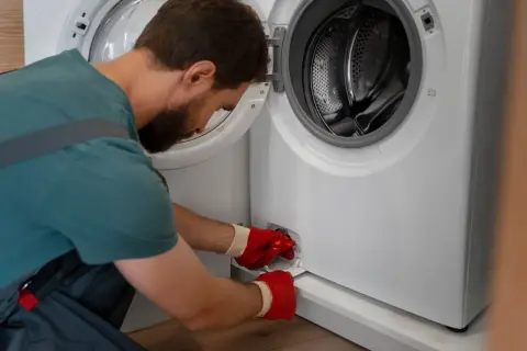 Mężczyzna w czerwonych rękawiczkach otwiera klapkę pralki, by sprawdzić, czym wyczyścić gumę.