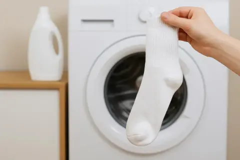 Dłoń trzyma białą skarpetkę przed pralką. Dowiedz się, jak prać białe skarpetki, by były nieskazitelnie czyste.