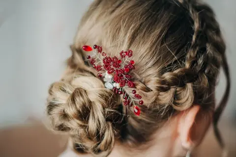 Eleganckie fryzury komunijne z warkoczem i ozdobą z czerwonych koralików. Delikatny warkocz oplata głowę, tworząc romantyczną całość.