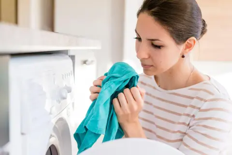 Kobieta wącha świeżo wyprane ubranie, zastanawiając się, dlaczego pranie śmierdzi po wysuszeniu.