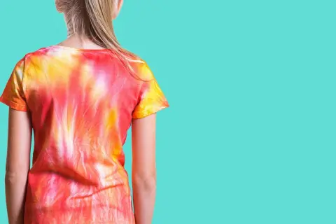 Dziewczynka w koszulce tie-dye w odcieniach czerwieni i żółci. To znaczy, że wzór powstał przez wiązanie i farbowanie materiału.
