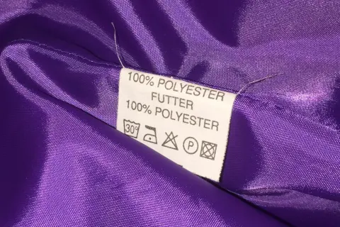 Metka z napisem "100% POLYESTER FUTTER" na fioletowej, błyszczącej podszewce. Czy poliester jest zdrowy? Pytanie pozostaje otwarte.