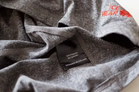 Szara koszulka z metką "92% Polyester 8% Spandex". Czy poliester się gniecie? Ta tkanina wygląda na odporną na zagniecenia.