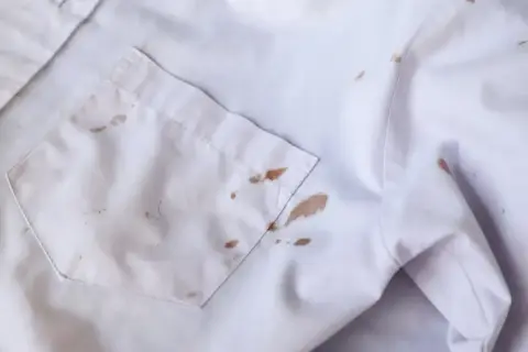 Biała koszula z brązowymi, trudne plamy na białych ubraniach. Wygląda jakby ktoś upuścił kawę lub czekoladę.