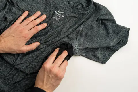 Dłonie czyszczą ciemną koszulkę Nike, by pozbyć się zapachu potu. Skuteczny sposób na świeżość ubrań sportowych.