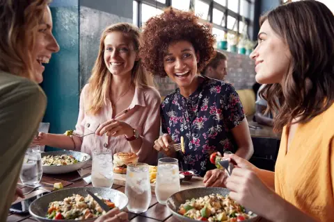Przyjaciółki śmieją się i jedzą w restauracji. Idealny pomysł na stylizację, jak się ubrać na babski wieczór.