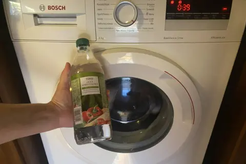 Dłoń trzyma butelkę octu spirytusowego przy pralce Bosch. Ocet do pralki to świetny sposób na odświeżenie bębna.
