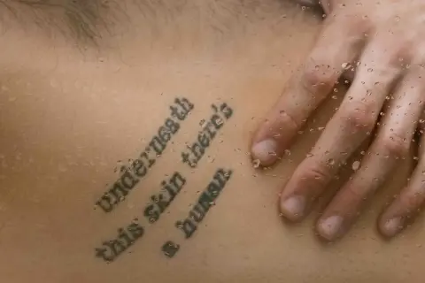 Mądre cytaty na tatuaż: "Underneath this skin there's a human". Dłoń na skórze z kroplami wody.
