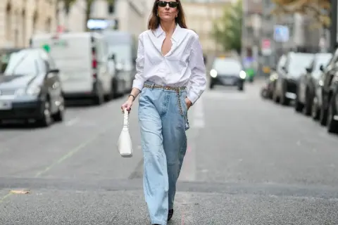 Kobieta w luźnych jeansach i białej koszuli, z białą torebką. To jest właśnie ten styl, który można nazwać "mom fit".