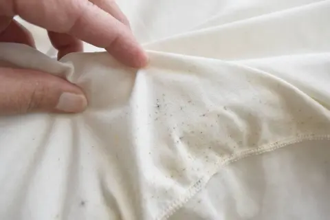 Dłoń pokazuje biały materiał z widocznymi, nieestetycznymi, tłustymi plamami na ubraniach po praniu.
