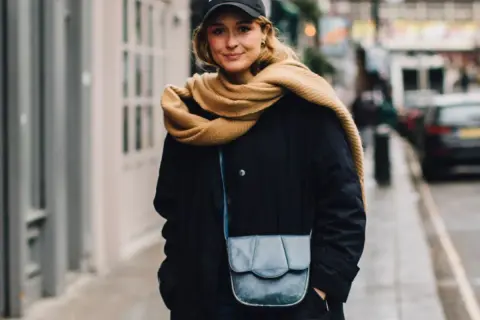 Kobieta w czapce i czarnej kurtce z kapturem, z beżowym szalikiem owiniętym wokół szyi. Stylowy sposób, jak wiązać szalik do kurtki z kapturem.