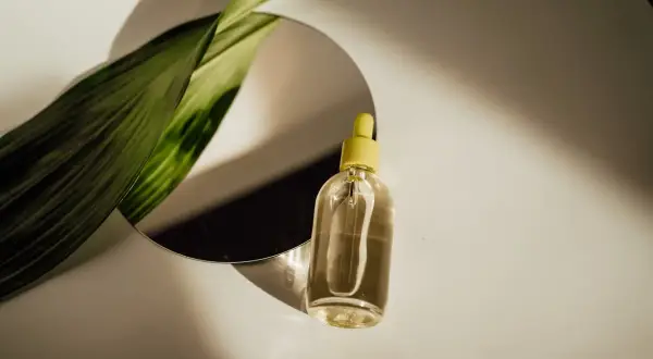 Szklana buteleczka z żółtą pipetką i zielony liść odbijają się w lustrze. Czy serum się zmywa? Naturalne piękno w kropli.