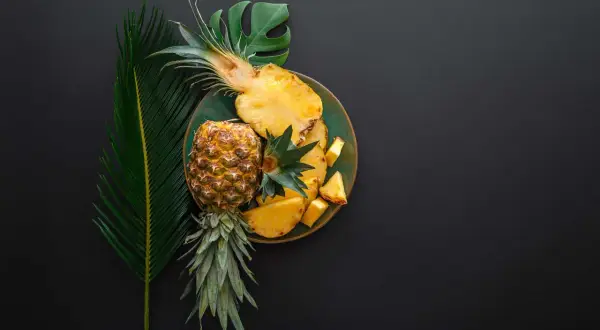 Ananas na talerzu, obok liści. Czy wiesz, że bromelaina co to za enzym? Pomaga w trawieniu.