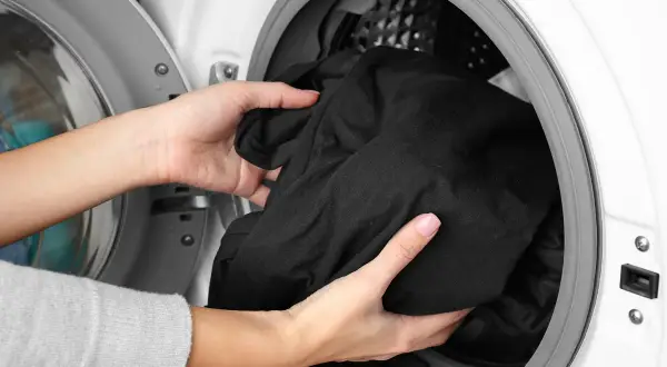 Ręce wkładają czarne pranie do pralki. Zastanawiasz się, dlaczego czarne pranie śmierdzi? Może to kwestia niewłaściwego prania.