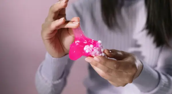 Różowy slime z białymi kuleczkami w dłoniach. Dowiedz się, jak usunąć slime z ubrania, zanim zaschnie.