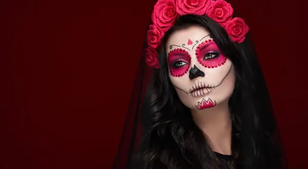 Kobieta z delikatnym makijażem na Halloween w stylu Catriny, ozdobiona czerwoną opaską z róż.