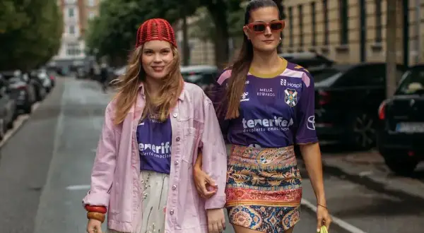 Dwie kobiety idą ulicą, prezentując, jak modnie się ubrać. Jedna w różowej kurtce i kwiecistej sukience, druga w sportowej koszulce i wzorzystej spódniczce.