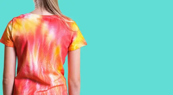 Dziewczynka w koszulce tie-dye w odcieniach czerwieni i żółci. To znaczy, że wzór powstał przez wiązanie i farbowanie materiału.