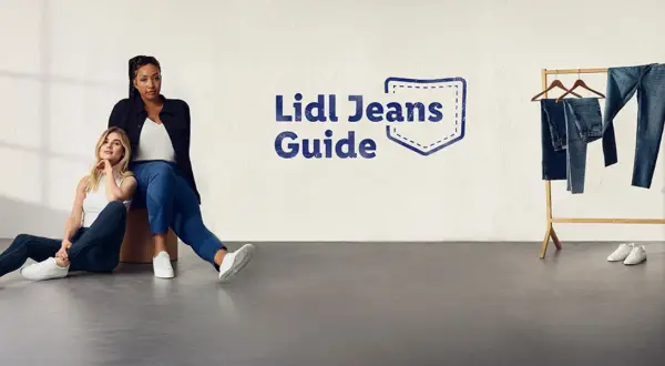 Dwie kobiety w jeansach siedzą na podłodze. Obok wieszak z jeansami. Rozmiar 27 jaki to rozmiar? Sprawdź w Lidl Jeans Guide.